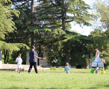 Joyful scene of children playing with bubbles in a sunny park surrounded by trees.