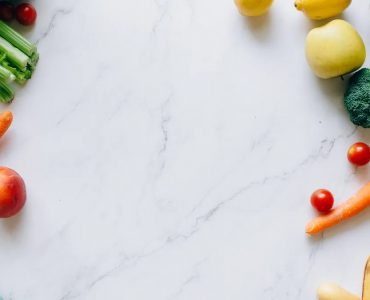 An assortment of fresh fruits and vegetables on a marble background, perfect for healthy lifestyle concepts.