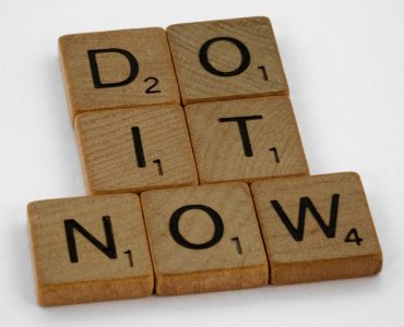 Wooden scrabble tiles forming 'DO IT NOW' on a minimal white backdrop. Inspiring concept.