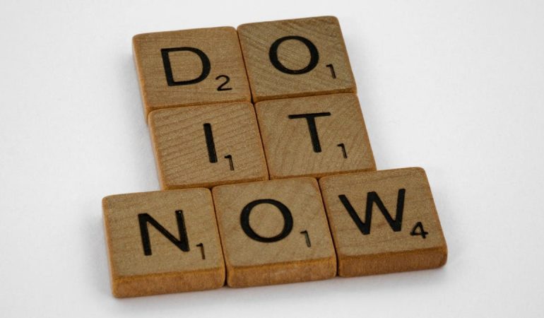 Wooden scrabble tiles forming 'DO IT NOW' on a minimal white backdrop. Inspiring concept.